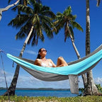Person relaxing in a hammock between palm trees with a clear blue sky and ocean view.