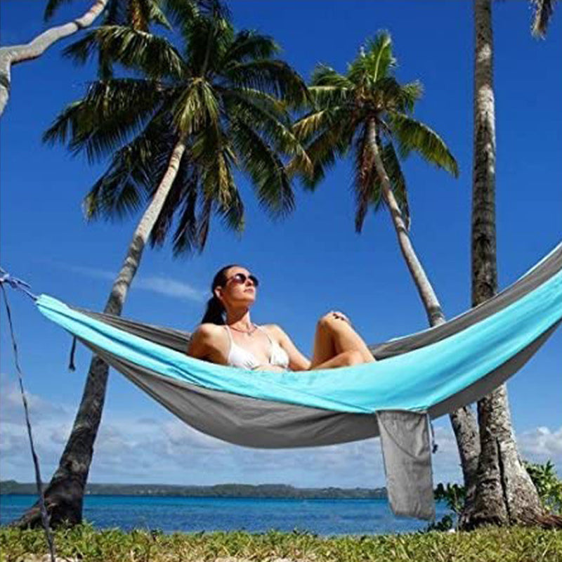 Person relaxing in a hammock between palm trees with a clear blue sky and ocean view.