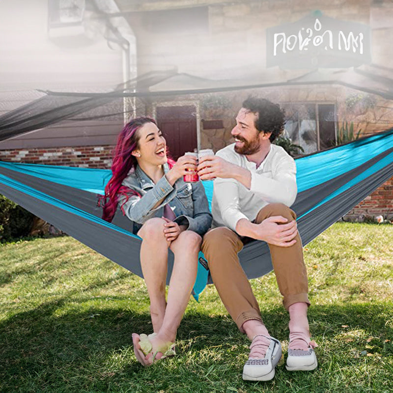 Two people sitting in a hammock outdoors, enjoying drinks together.