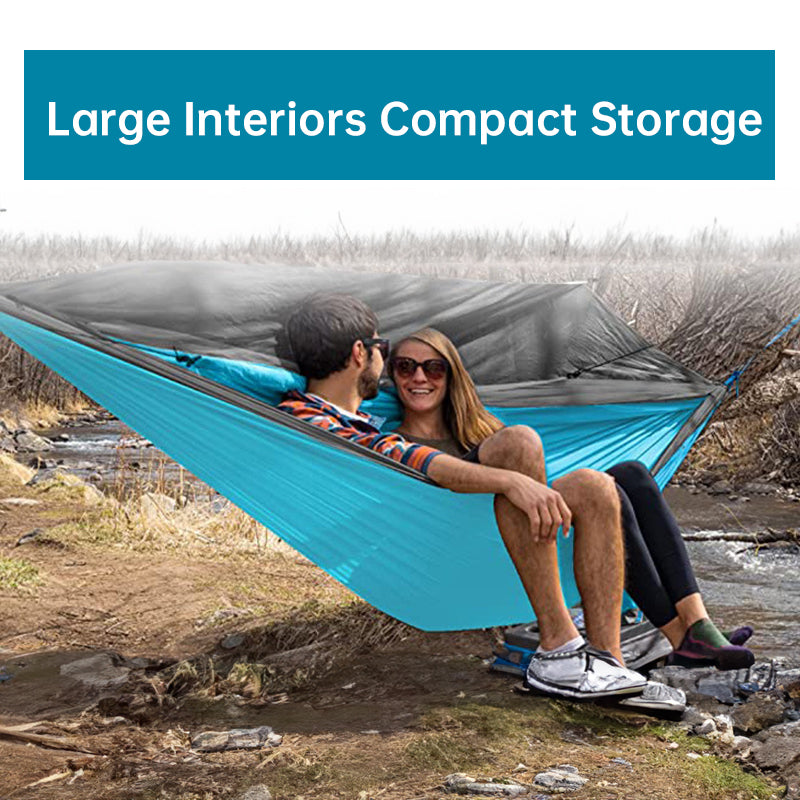 Two people sitting in a blue hammock with a mesh screen, surrounded by nature.