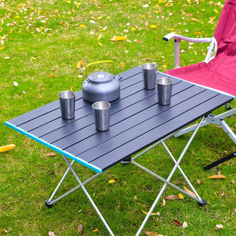 Camping table with a teapot and cups on a grassy outdoor setting