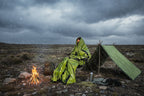 Person inside in a green emergency bivvy bag with two additional green bags and their storage cases.