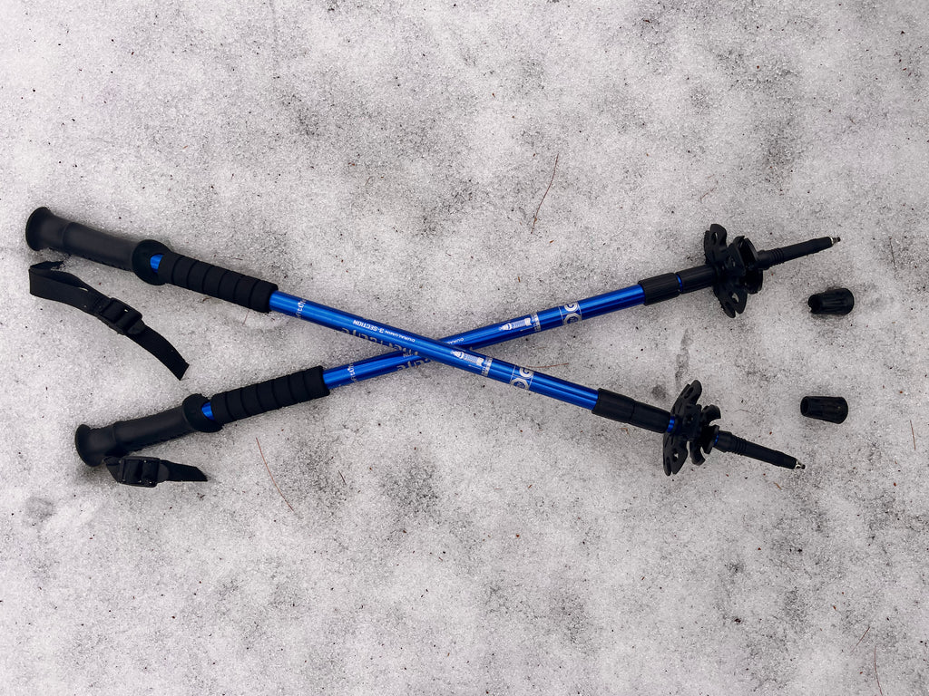 Two blue hiking poles with black grips on a snowy surface - offered by the premier hiking and climbing gear store in the Northeastern United States, The Adirondack Tool Co.