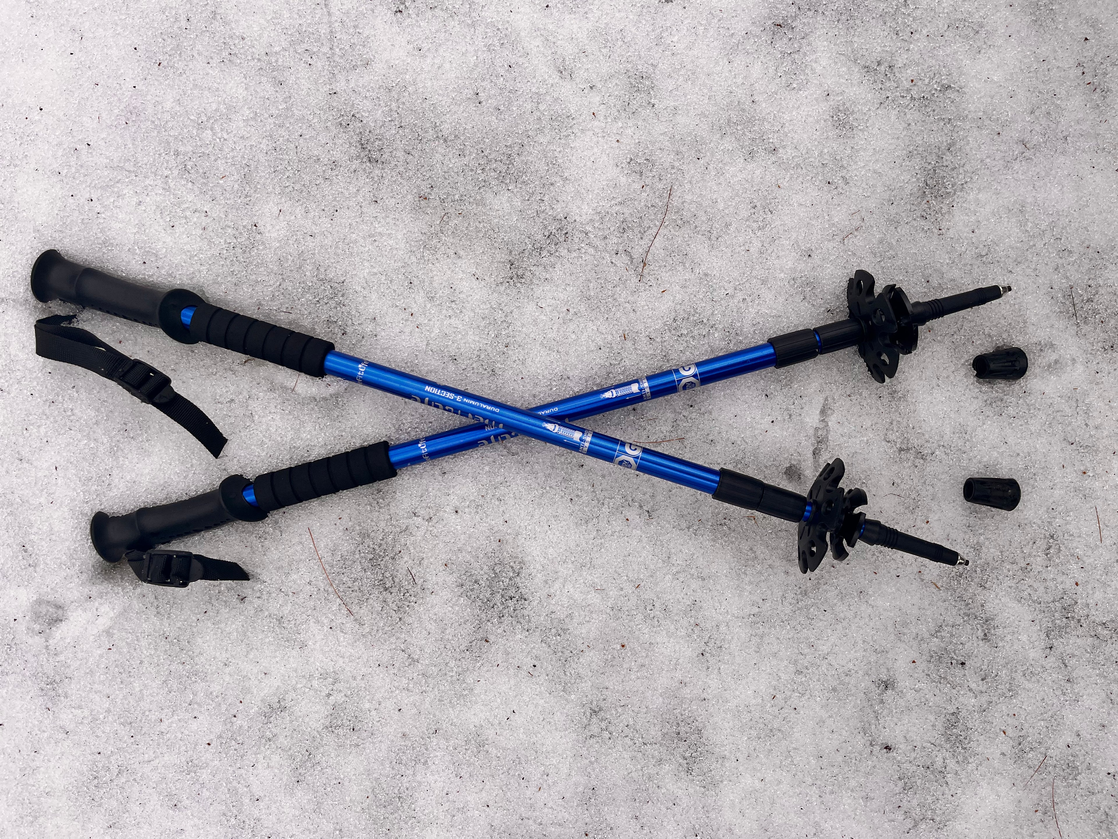 Two blue hiking poles with black grips on a snowy surface - offered by the premier hiking and climbing gear store in the Northeastern United States, The Adirondack Tool Co.