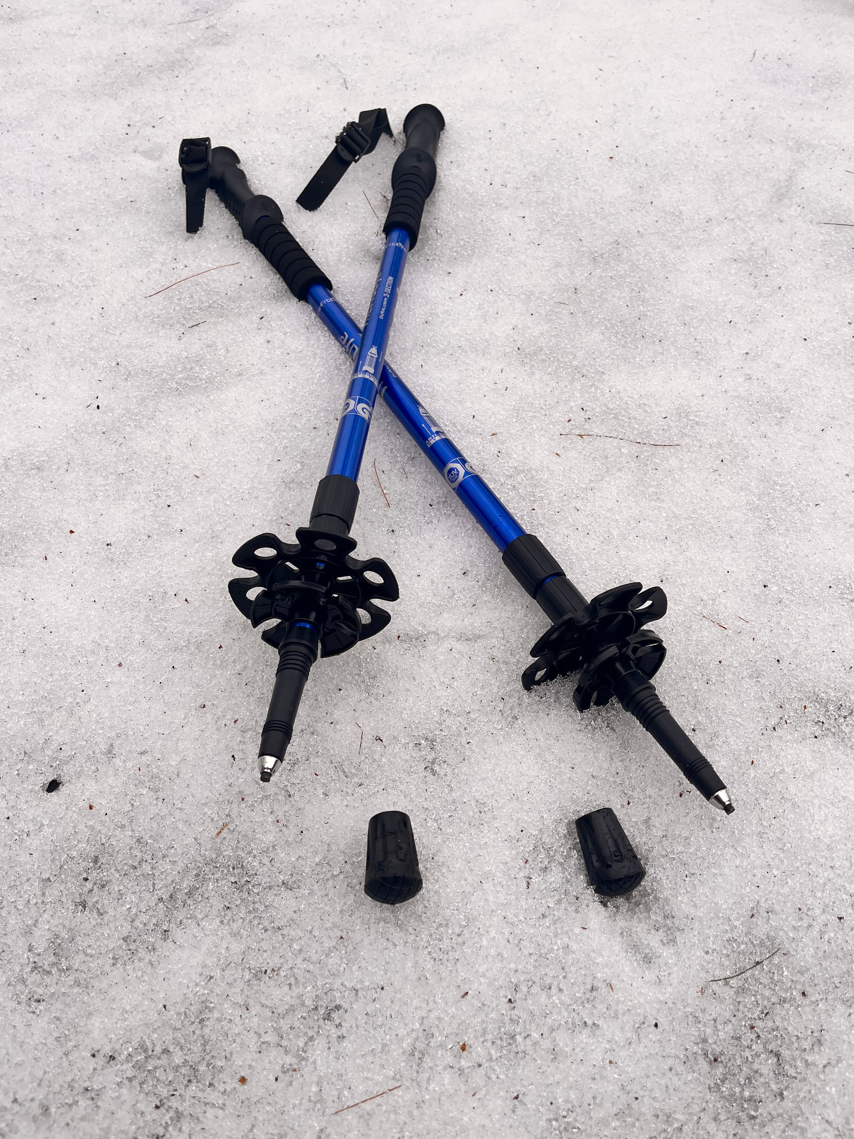 Two blue and black hiking poles on a snowy surface - offered by the premier hiking and climbing gear store in the Northeastern United States, The Adirondack Tool Co.