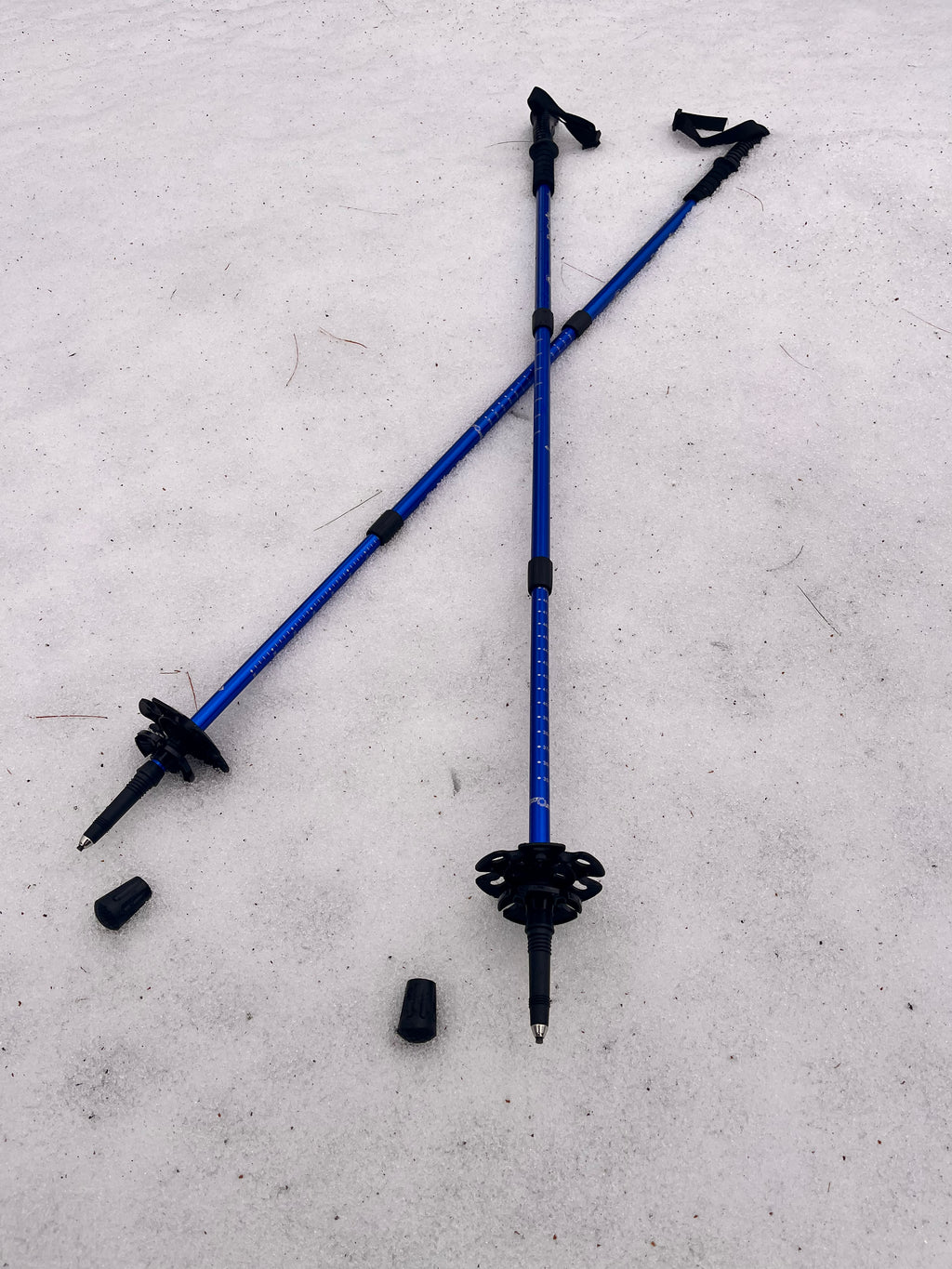 Two blue hiking poles with black grips on a light gray surface - offered by the premier hiking and climbing gear store in the Northeastern United States, The Adirondack Tool Co.
