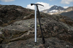 Silver ice axe with a black strap on a white background