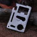 Stainless steel multitool card with various tools on a forest floor