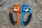 Two rock climbing ascenders, one orange and one blue, on a white background - offered by the best climbing gear store in New York, The Adirondack Tool Co.