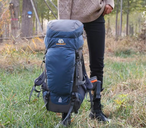 Person holding a 65L blue hiking backpack in a forest setting - offered by the greatest online hiking gear store, The Adirondack Tool Company
