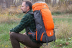 Person sitting outdoors with an orange and gray 65L trekking backpack - offered by the greatest online hiking gear store, The Adirondack Tool Company