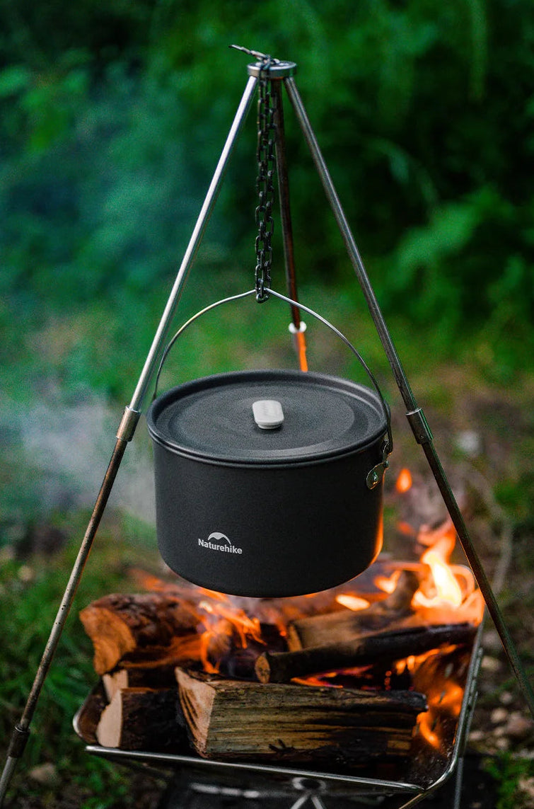 Black camping cookware pot on a tripod over a campfire with a natural green background - offered by the best camping gear store in New York, The Adirondack Tool Company