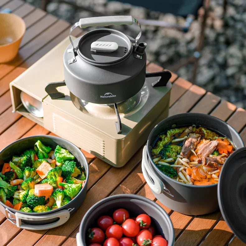 Outdoor cooking setup with a portable stove and camping cookware pots, and fresh vegetables on a wooden table - offered by the best camping gear store in New York, The Adirondack Tool Company