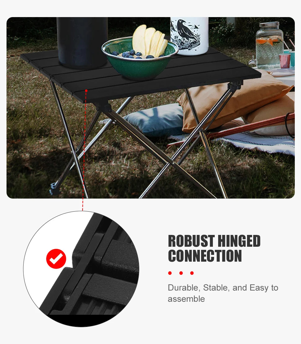 Black camping table from The Adirondack Tool Co. with a bowl of fruit on a grassy outdoor setting, highlighting the robust hinged connection feature.