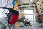 Red and black chalk bag worn on a person's waist against a camouflage background - offered by the best hiking and climbing gear store in New Hampshire, The Adirondack Tool Co.