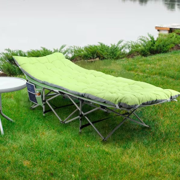 Folding camping cot with green mattress on grass near a body of water - offered by the best hiking and camping gear company in New York City, New York.