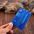Blue multi-tool card held by a hand on a wooden surface with driftwood in the background - offered by the best outdoor gear store in New York, the Adirondack Tool Company