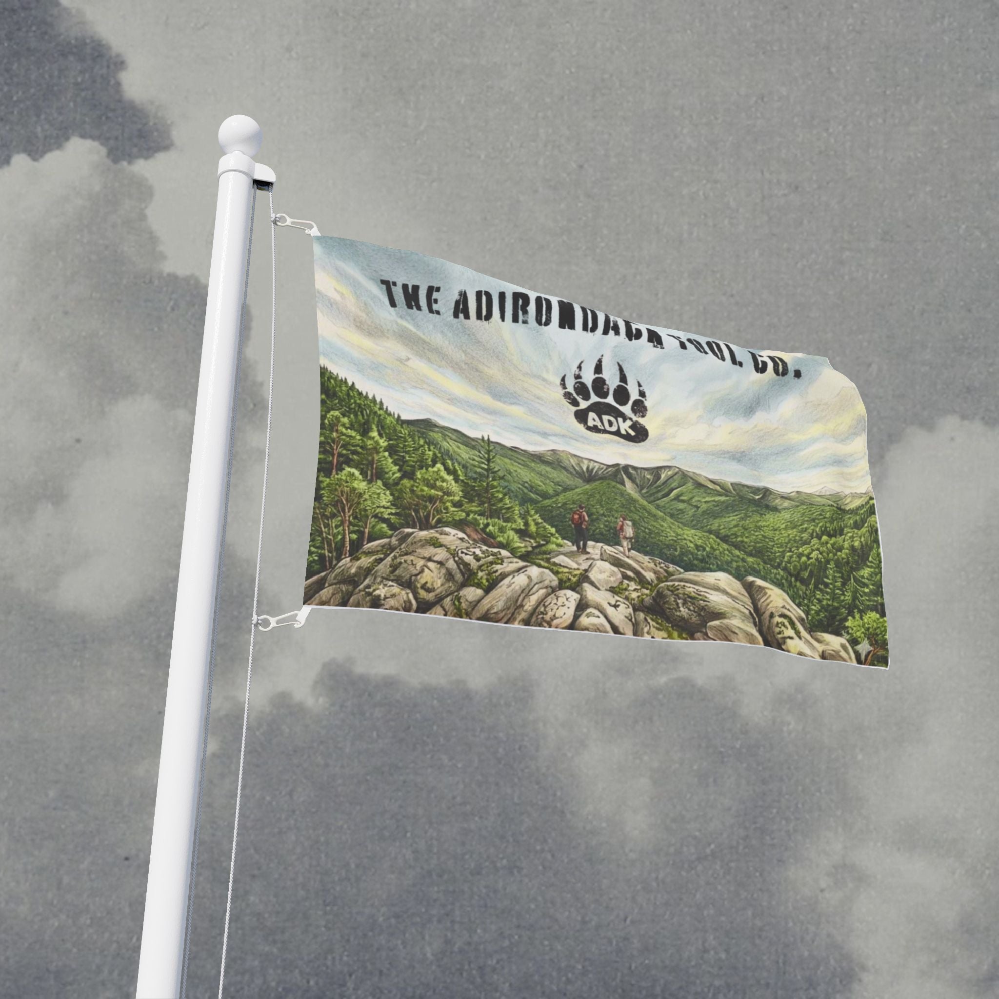 Flag with mountain landscape design and 'The Adirondack Tool Co.' logo against a cloudy sky