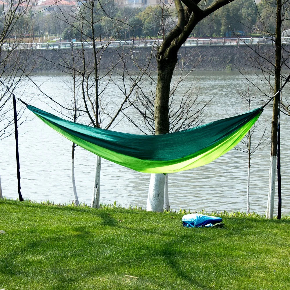 Green hammock hanging between trees by a lake - offered by the best camping gear store in the northeast, the Adirondack Tool Co.