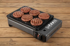 Portable gas-powered grill with food on a white background by The Adirondack Tool Co. 