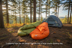 Two sleeping bags from The Adirondack Tool Co., one green and one orange, zipped together on a camping background