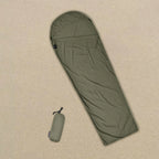 Olive green sleeping bag with a matching carrying bag on a tent floor background - offered by the best camping gear store in New York, The Adirondack Tool Co.
