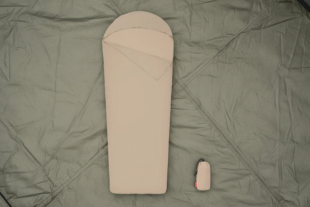 Beige sleeping bag with a matching carrying bag on a tent floor background - offered by the best camping gear store in New York, The Adirondack Tool Co.