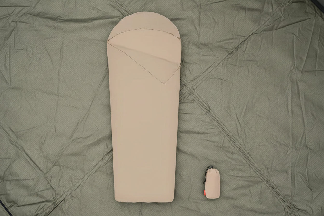 Beige sleeping bag with a matching carrying bag on a tent floor background - offered by the best camping gear store in New York, The Adirondack Tool Co.