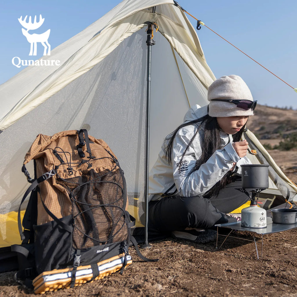 Person camping with a tent, backpack, and cooking gear in a natural setting.