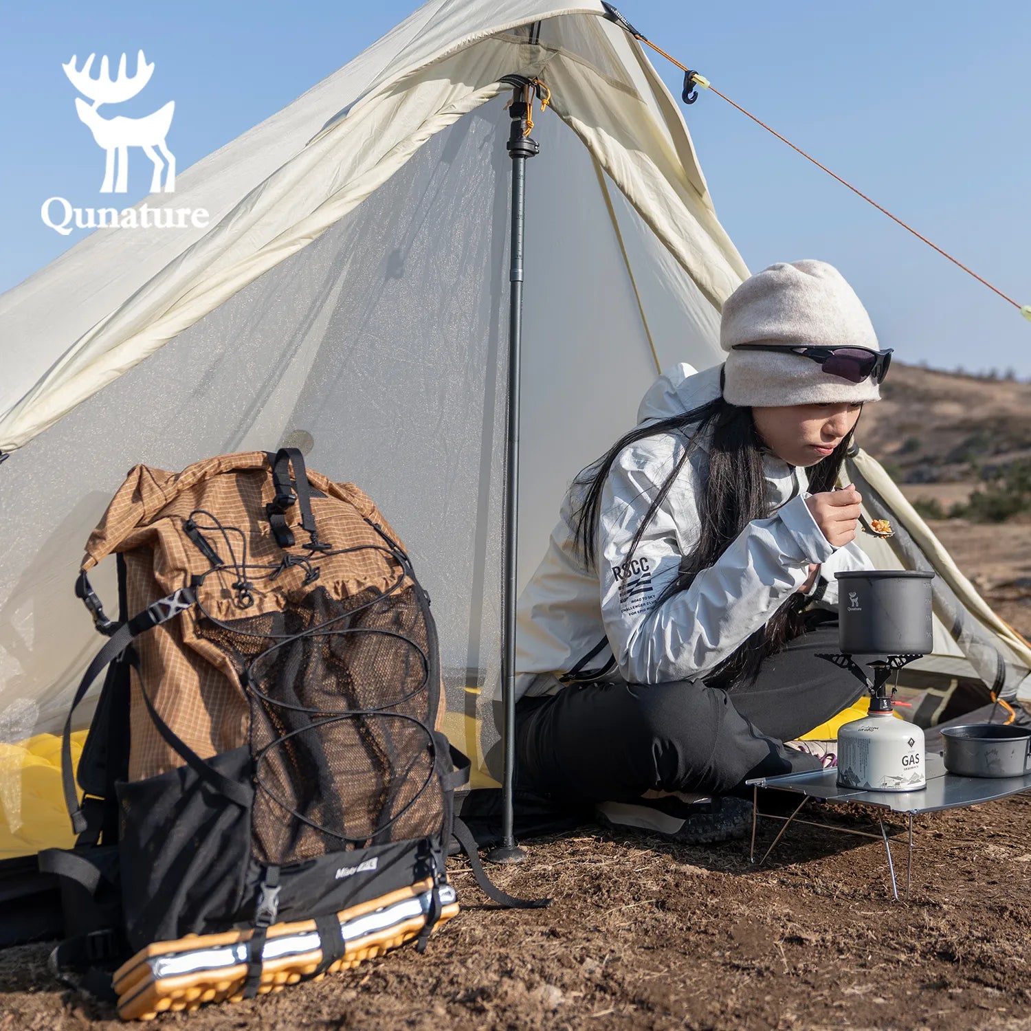 Person camping with a tent, backpack, and cooking gear in a natural setting.